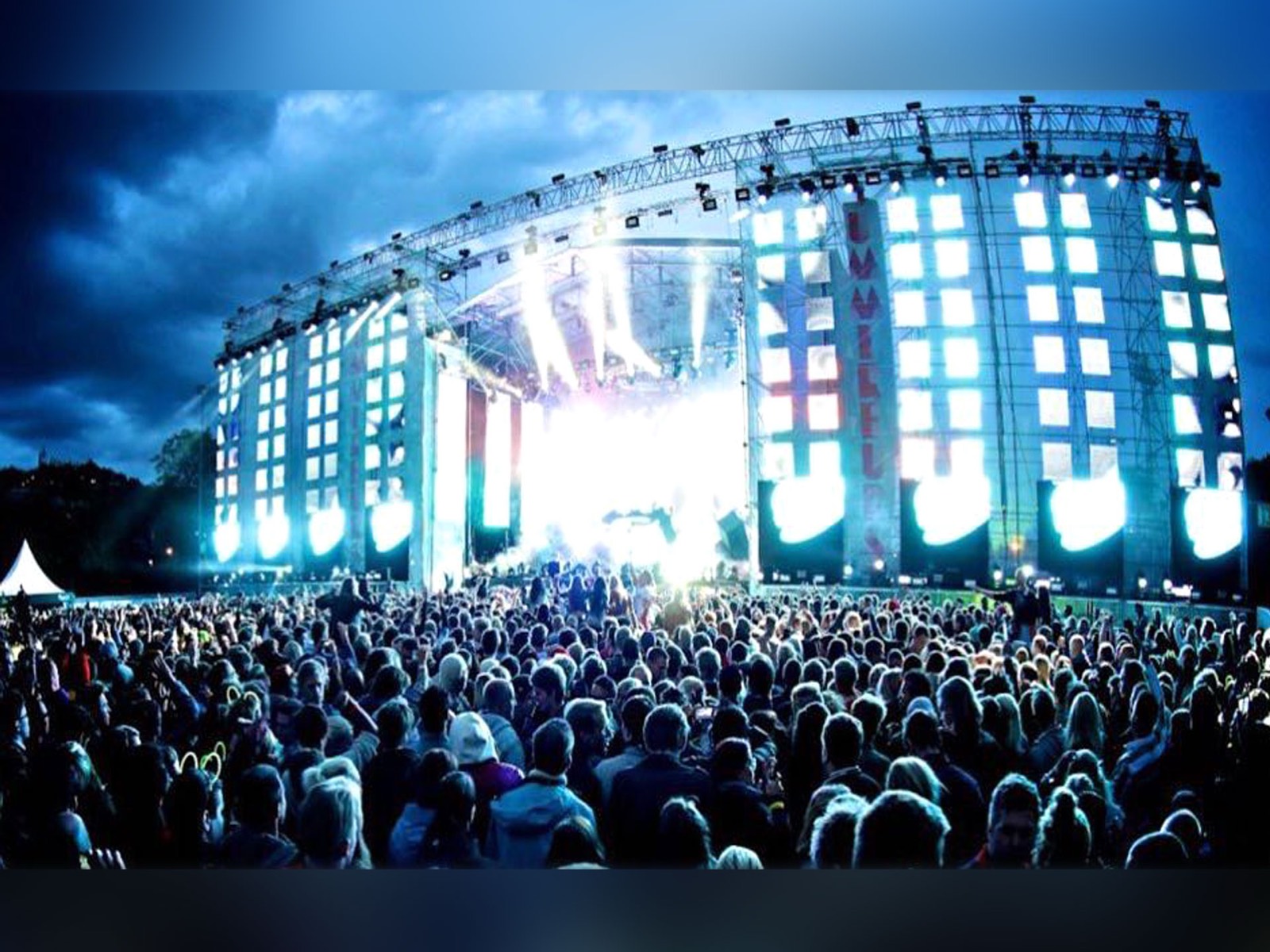 Festival main stage at dusk: LED columns playing show content above a packed crowd