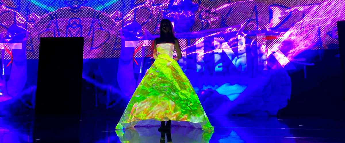 A model in a white gown lit by projection-mapped neon graphics on a runway
